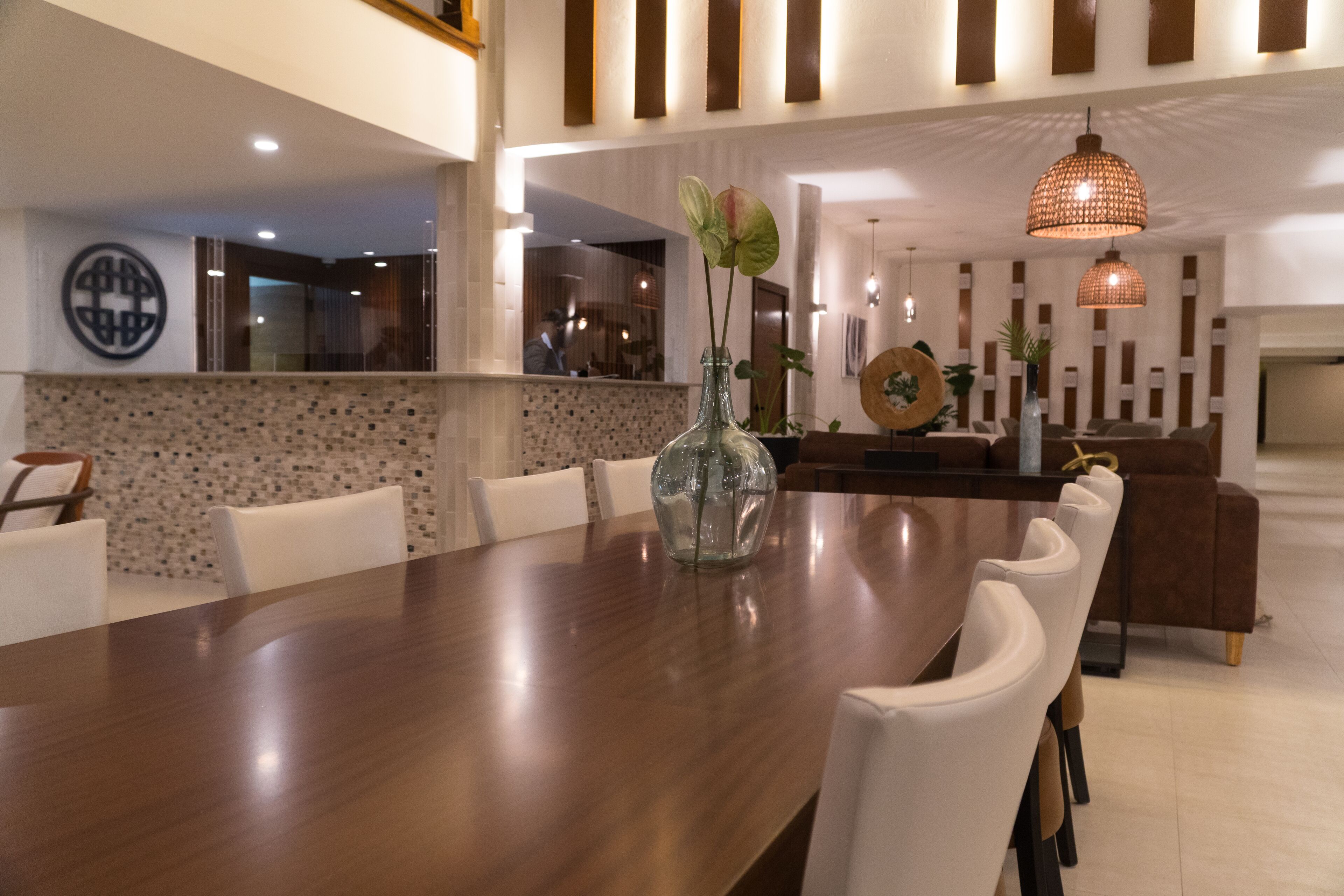 Un espace repas moderne avec une longue table en bois, des chaises blanches et un vase décoratif.