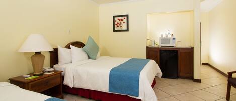 A hotel room with two beds, a desk with a microwave, and a bathroom visible through an open door.