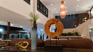 A modern lobby with a glass coffee table, a potted plant, a wooden sculpture, and a staircase in the background. - Cara Hotels Trinidad (Claxton Bay)