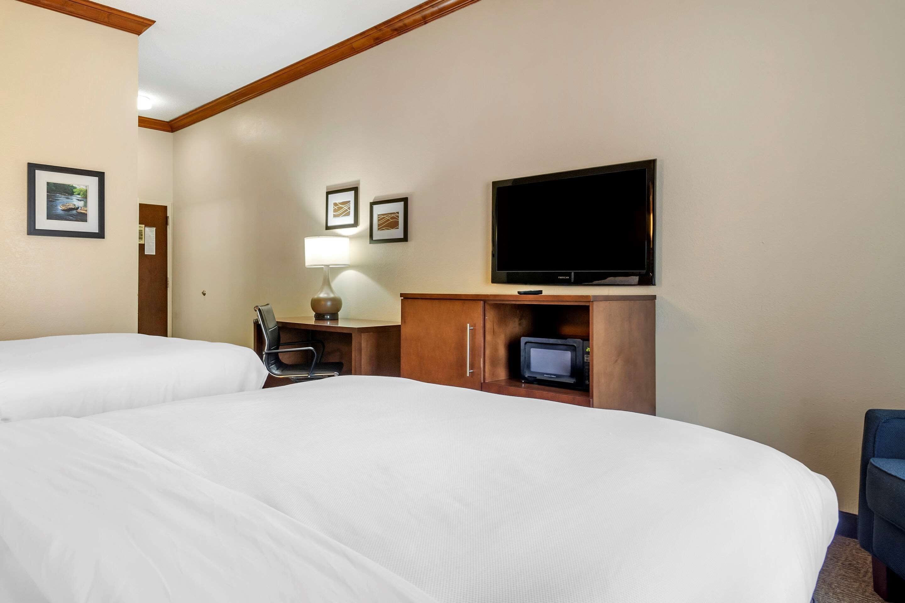 A hotel room with two beds, a television, a desk with a lamp, and framed pictures on the wall.