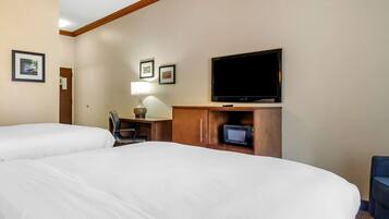 A hotel room with two beds, a television, a desk with a lamp, and framed pictures on the wall.
