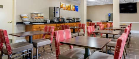 A restaurant with multiple tables and booths, equipped with kitchen appliances and a flat-screen TV on the wall.