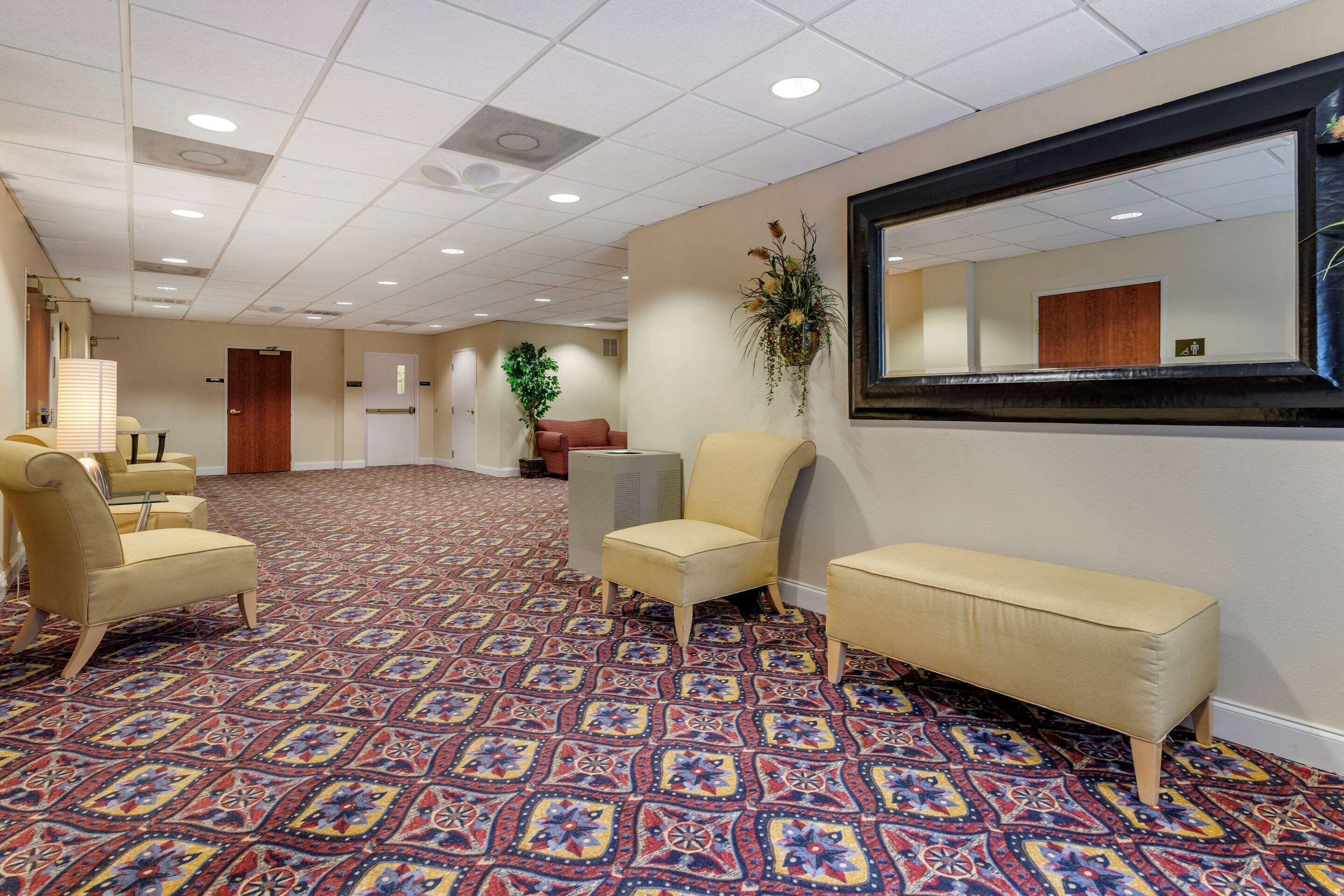 A spacious hotel lobby with patterned carpet, multiple seating areas, and a large mirror on the wall.