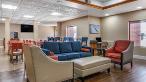 A hotel lobby with a blue sofa, beige armchair, and red armchair. There is a TV on the wall, a fireplace, and a window with a view of the outside. - Comfort Inn & Suites Statesboro - University Area (Statesboro)