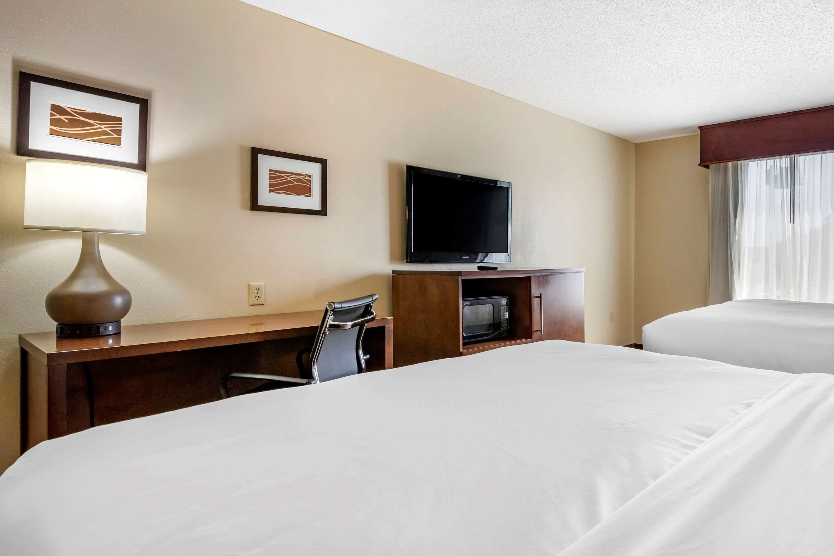 A hotel room with two beds, a desk with a lamp, a television, and framed artwork on the wall.