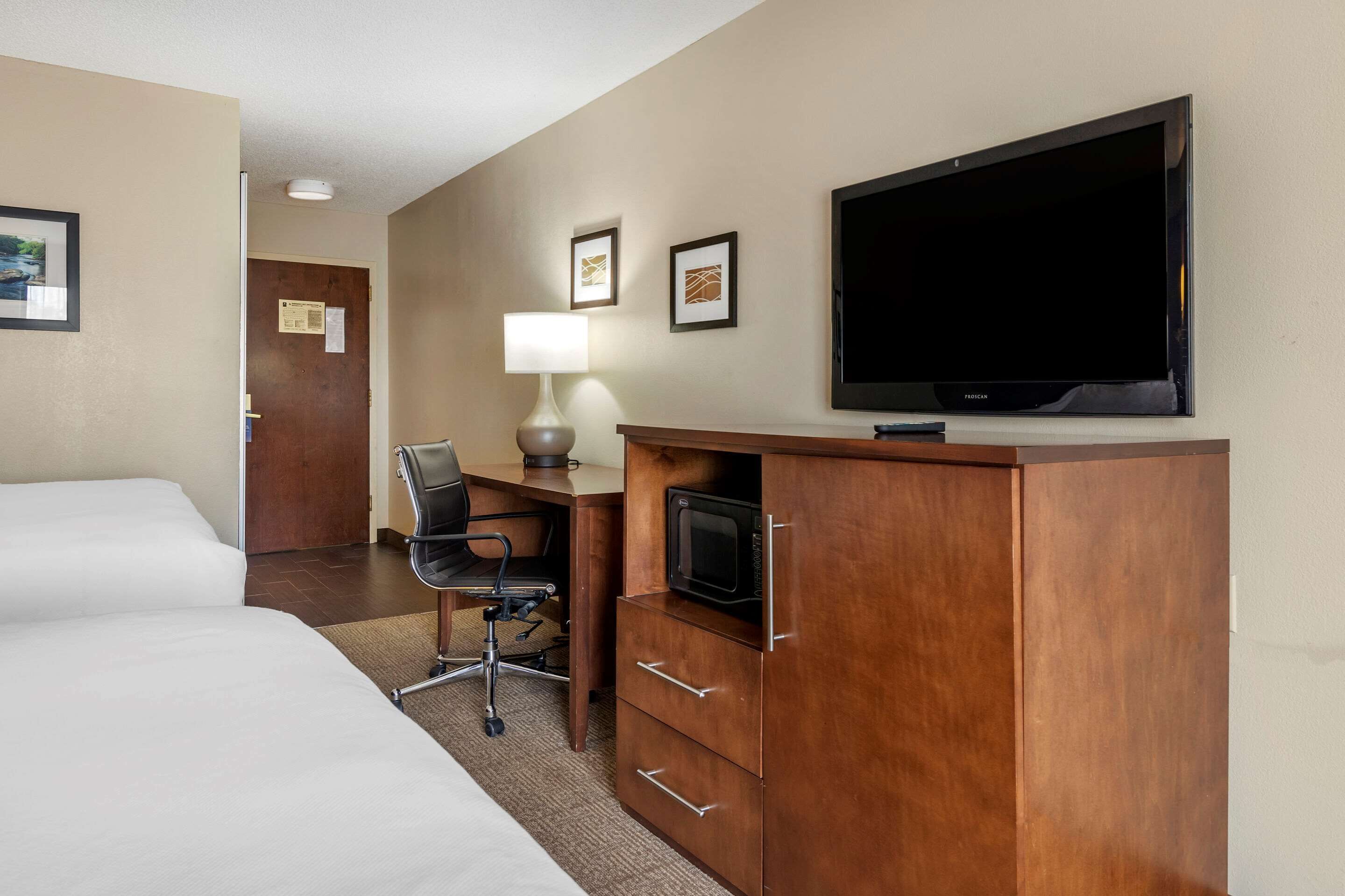 A hotel room with two beds, a desk with a chair, a flat-screen TV, and a microwave.