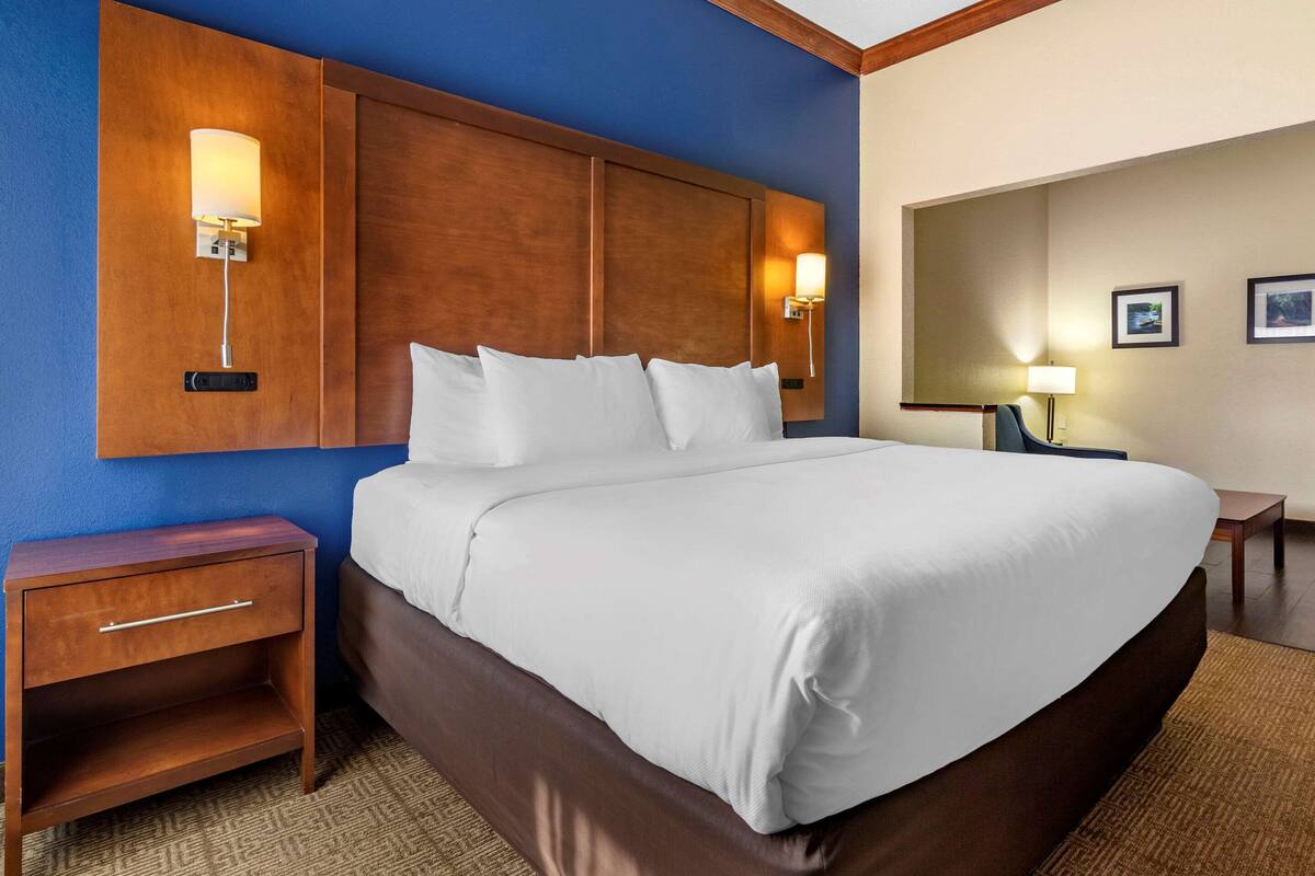 Une chambre d’hôtel dotée d’un grand lit, d’une tête de lit en bois, de tables de chevet et de lampes fixées au mur.