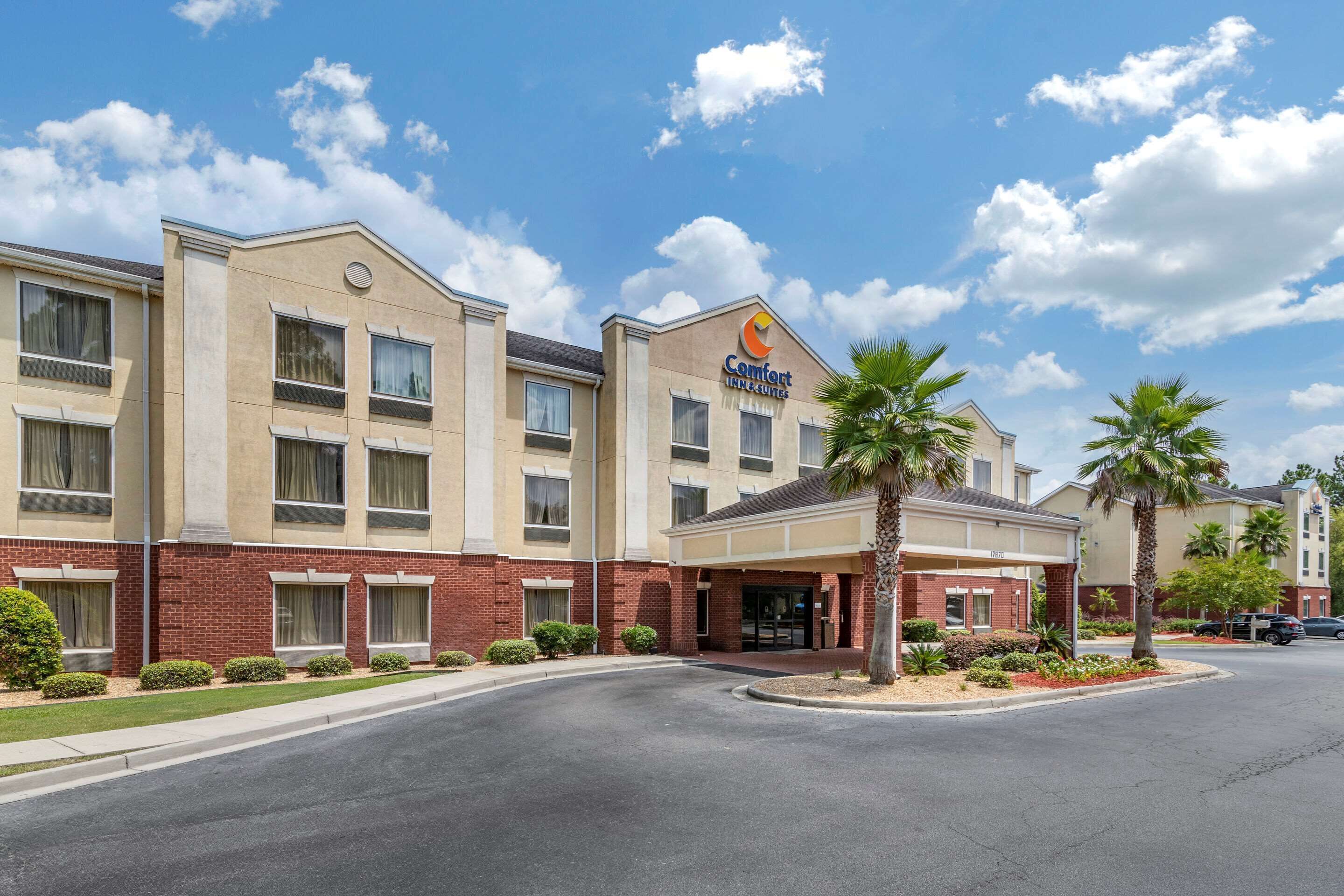 Ein Comfort Inn & Suites Hotel mit Backsteinfassade, zahlreichen Fenstern und einem begrünten Eingangsbereich mit Palmen.