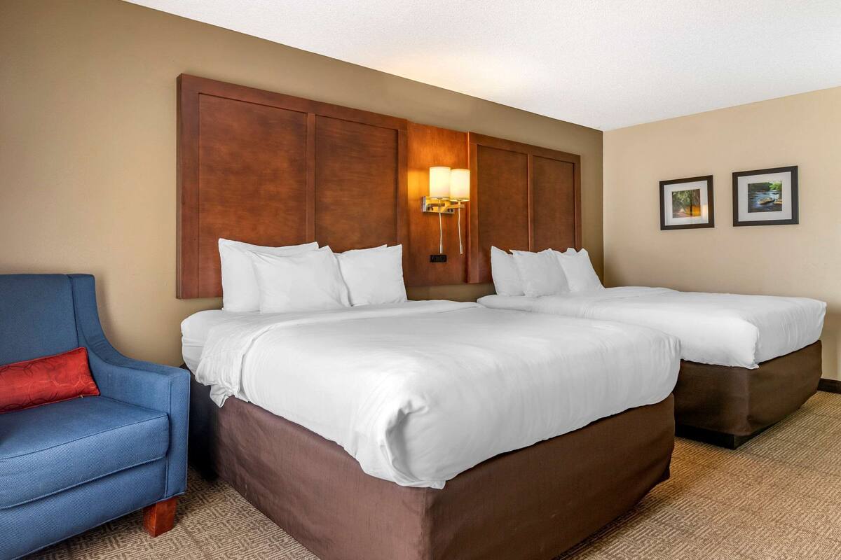 Une chambre d’hôtel avec deux lits, un fauteuil bleu et une lampe fixée au mur.