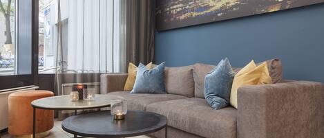 A modern living area with a sofa, a round table, and a cityscape painting on the wall.