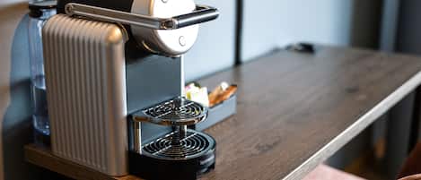 Una máquina de café Nespresso sobre una mesa de madera, con un vaso de agua y un pastel.