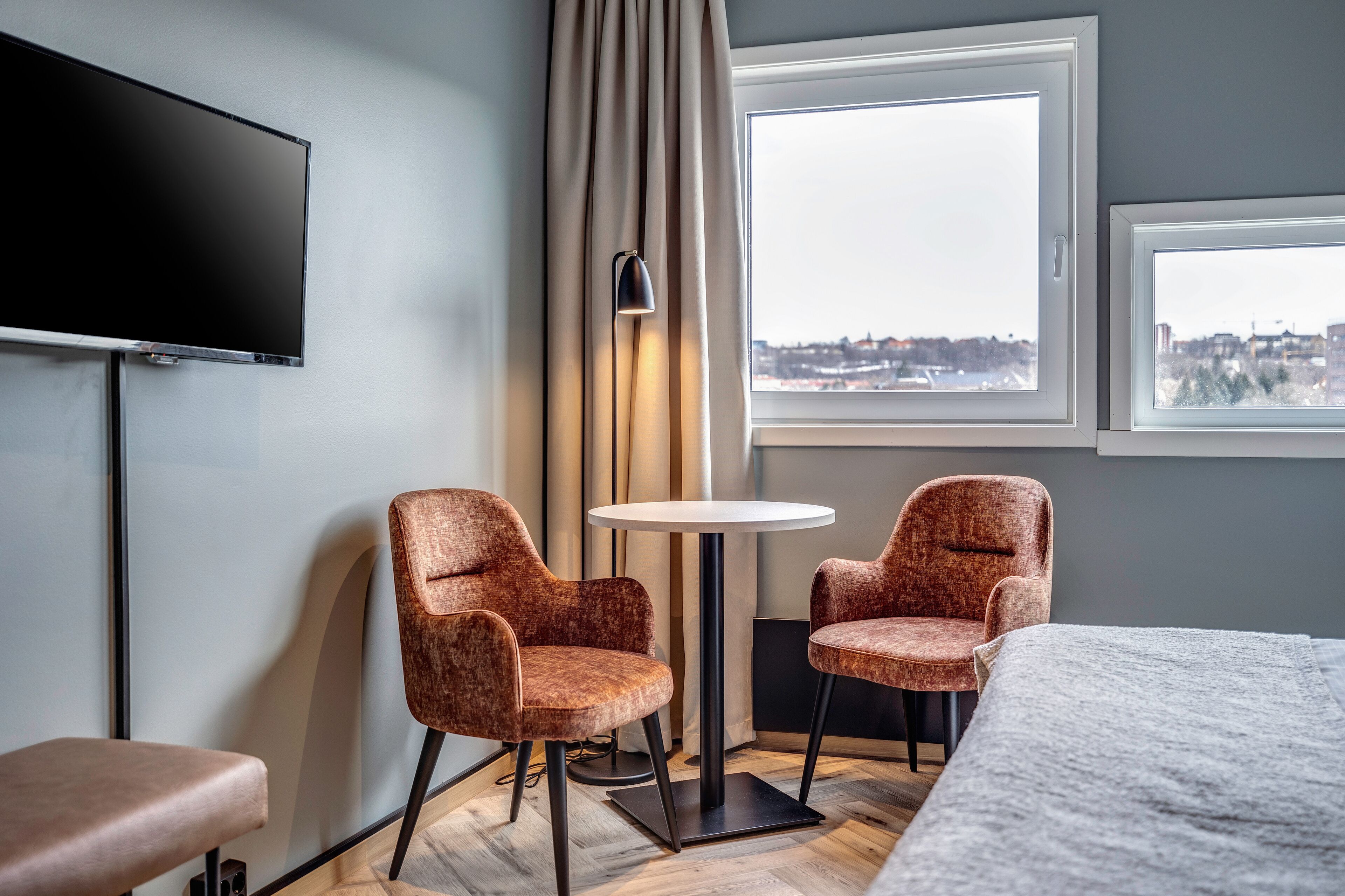 Habitación de hotel con cama, dos sillones, una mesita, televisión y ventana con vista a la ciudad.