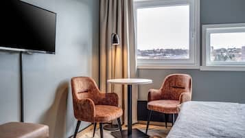 Habitación de hotel con cama, dos sillones, una mesita, televisión y ventana con vista a la ciudad.