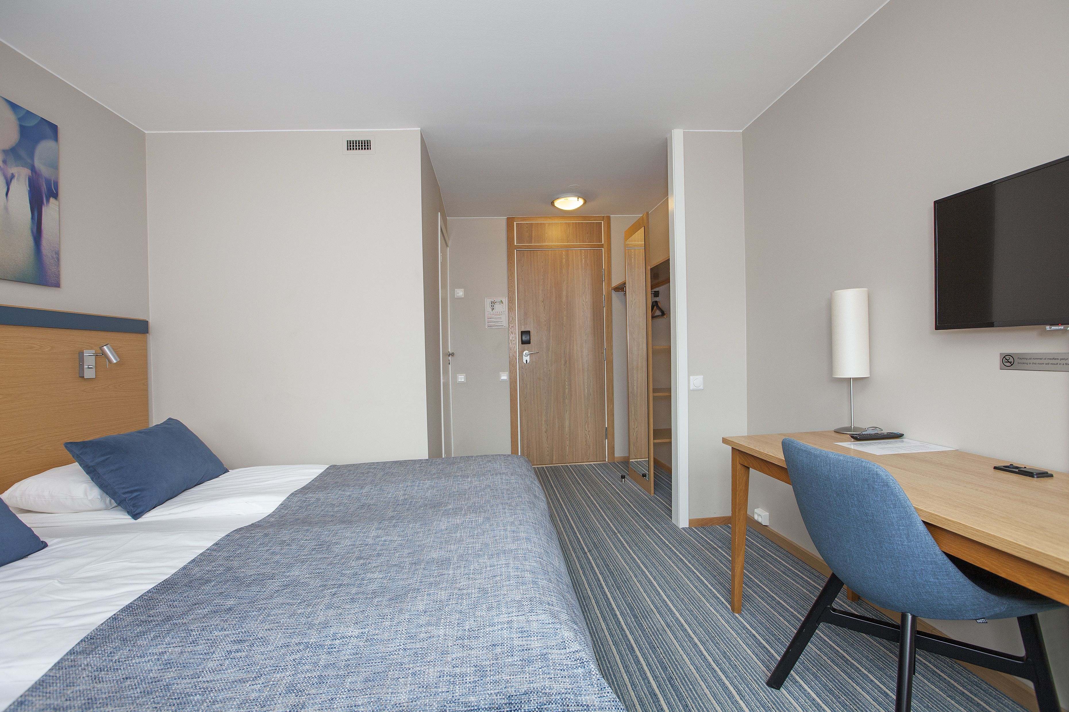 A hotel room with a bed, a desk, and a television.