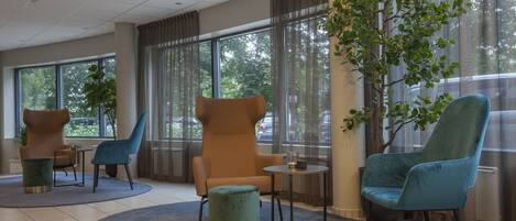 A modern lobby with seating arrangements, large windows, and a potted plant.