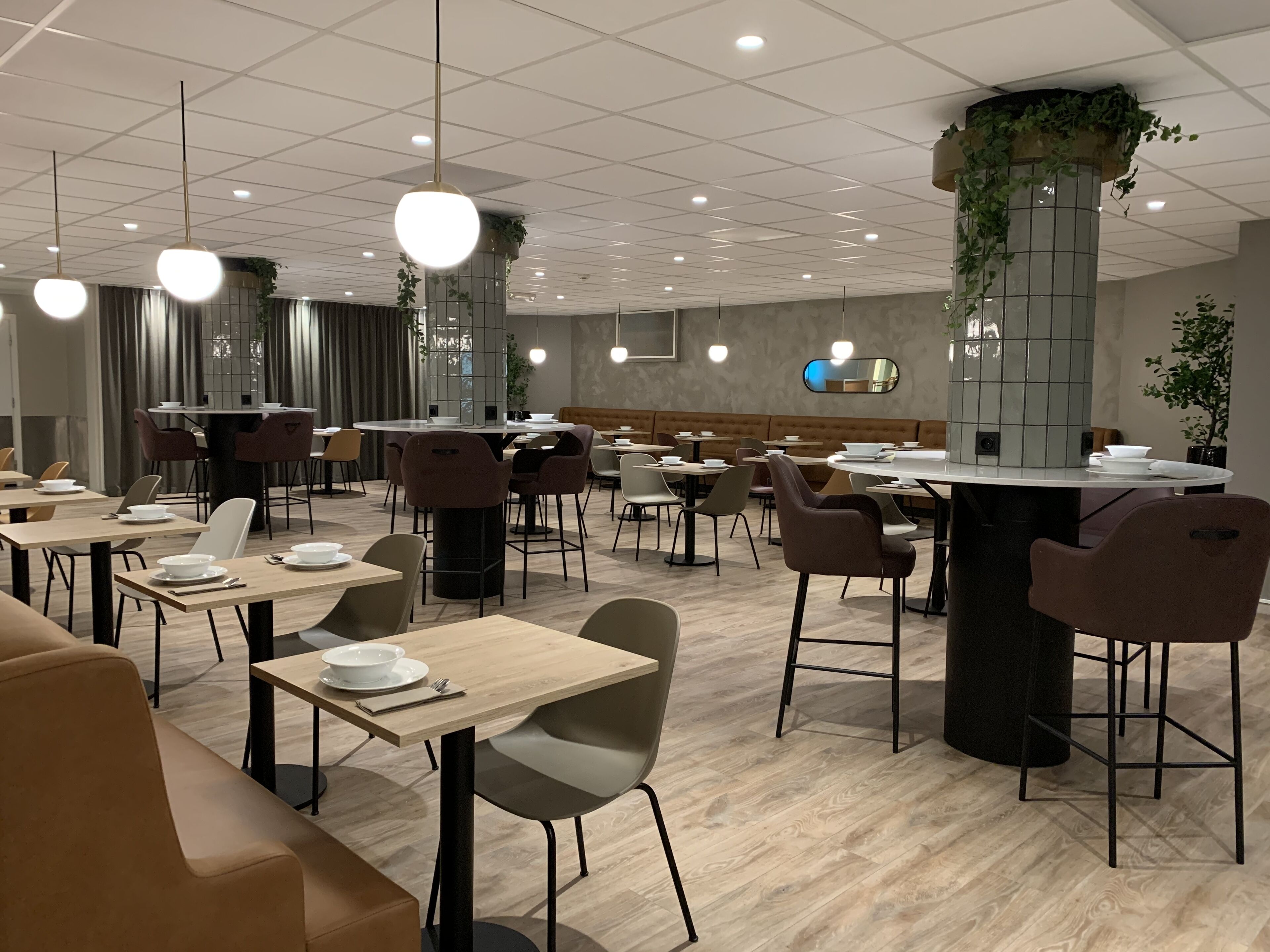 A modern restaurant with round tables, cushioned seating, and hanging plants.