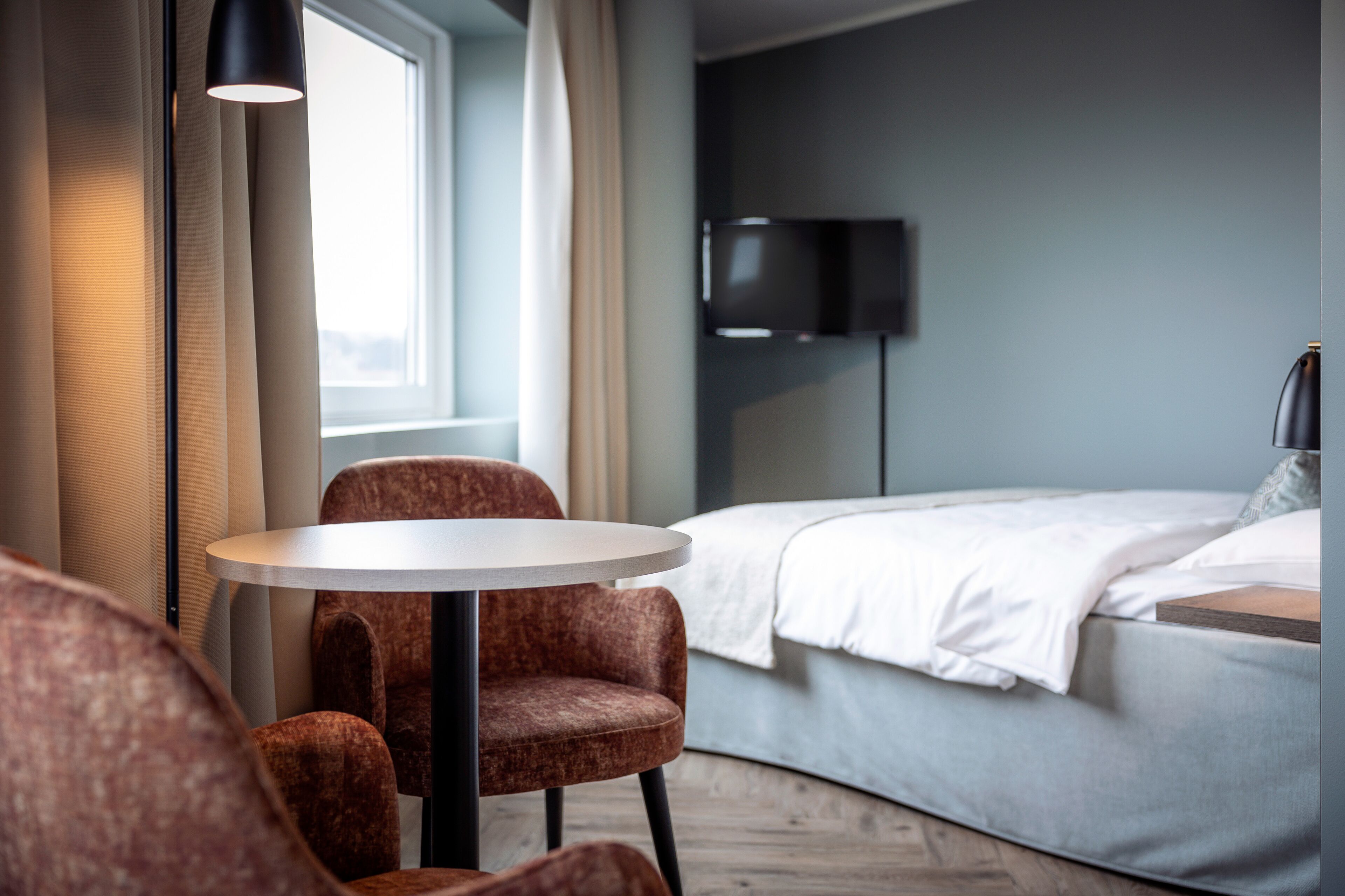 A modern hotel room with a bed, a round table, and two chairs.