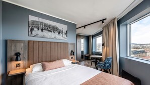 A modern hotel room with a large bed, a dining area, and a city view. - Anker Hotel (Oslo)