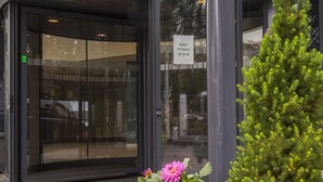 The entrance to the Anker Hotel with a glass door, a sign indicating the night entrance, and a potted plant with pink and white flowers. - Anker Hotel (Oslo)