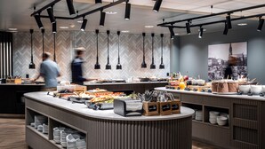 A modern buffet setup with a central island, multiple serving stations, and a herringbone-patterned wall. - Anker Hotel (Oslo)