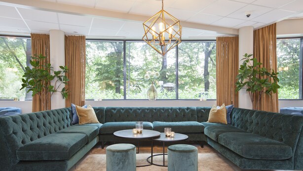A modern living room with a sectional sofa, two ottomans, a round coffee table, and a chandelier. - Anker Hotel (Oslo)