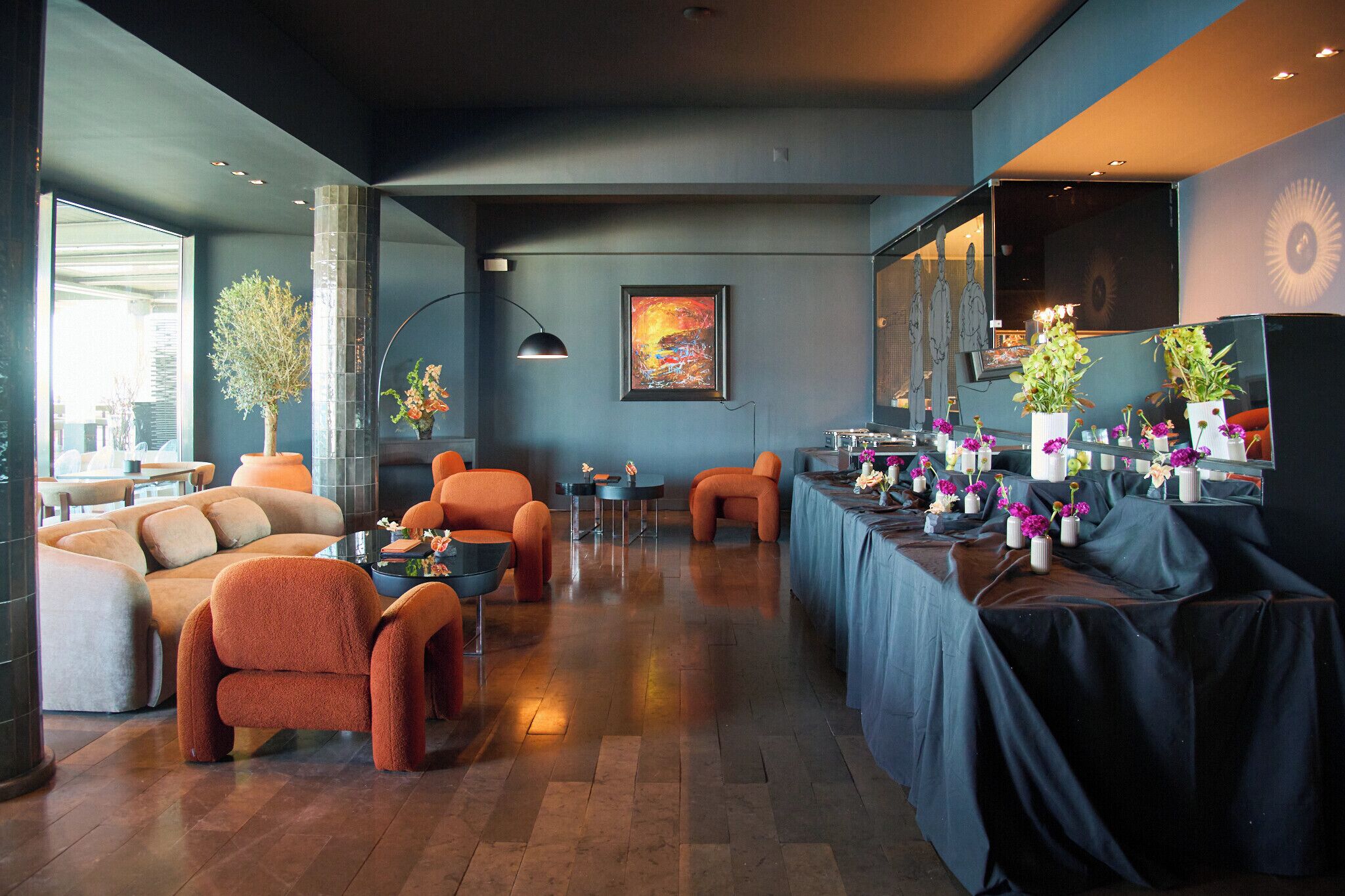 A modern lounge area with sofas, armchairs, a table with floral centerpieces, and a large abstract painting on the wall.