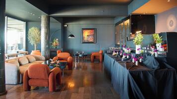 Un espace de détente moderne, avec des canapés, des fauteuils, une table agrémentée de compositions florales et un grand tableau abstrait accroché au mur.