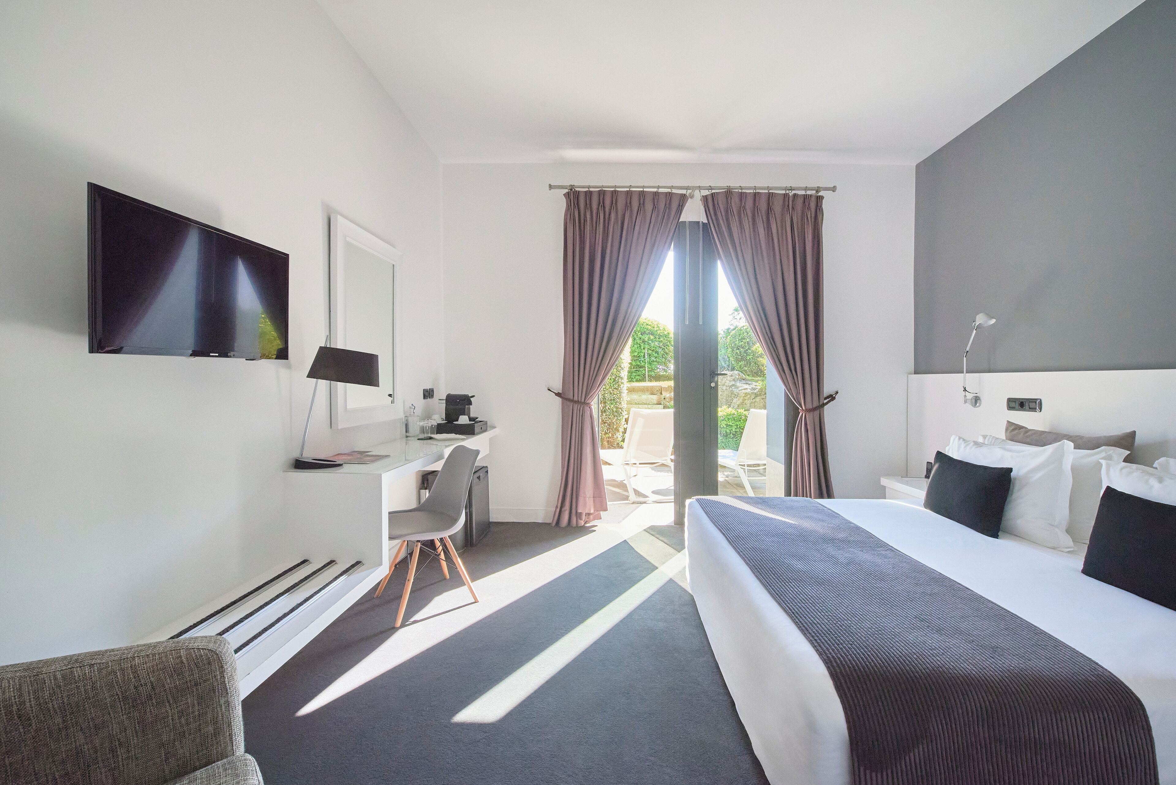 A modern hotel room with a large bed, a desk, a flat-screen TV, and a view of the outdoors.