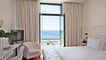 Habitación de hotel con cama, escritorio con televisor, silla y balcón con vista al mar.