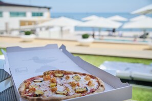 Una pizza en una caja, con una piscina y sombrillas al fondo.