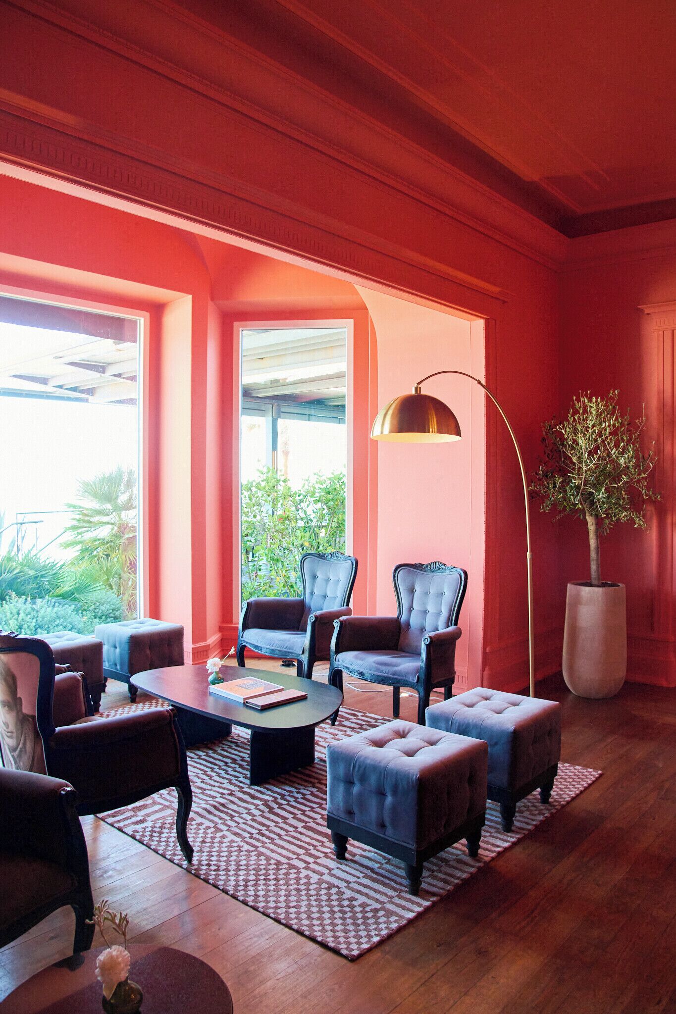 A room with a large window, a round table, two blue armchairs, a floor lamp, and a potted plant.