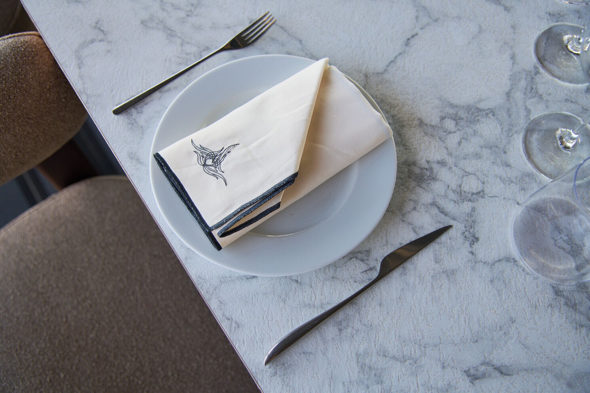 A table with a folded napkin, a fork, a knife, and a glass on a marble surface.