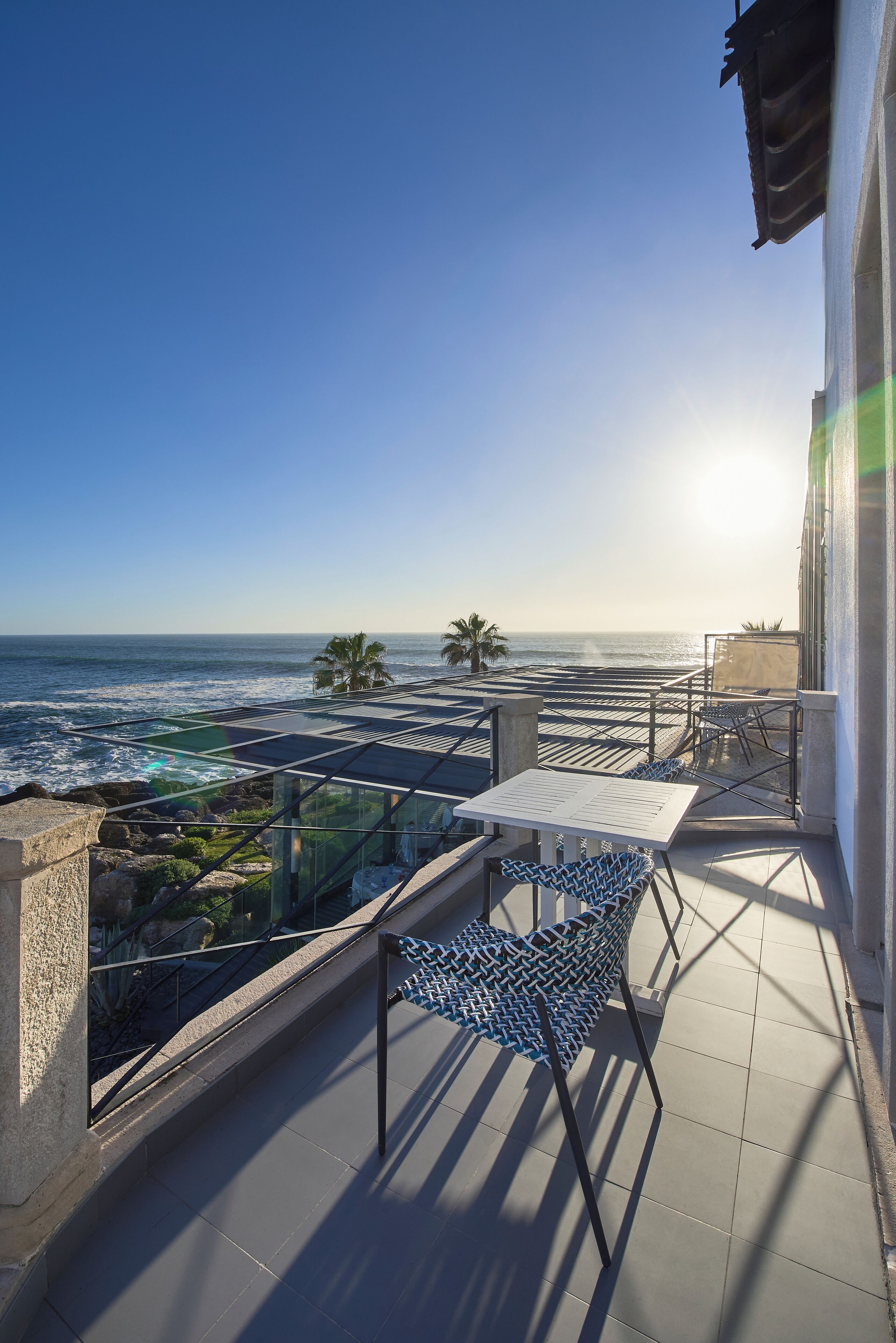 A balcony with a glass railing overlooking the ocean, a table, and chairs.