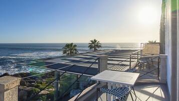 A balcony with a glass railing overlooking the ocean, a table, and chairs.