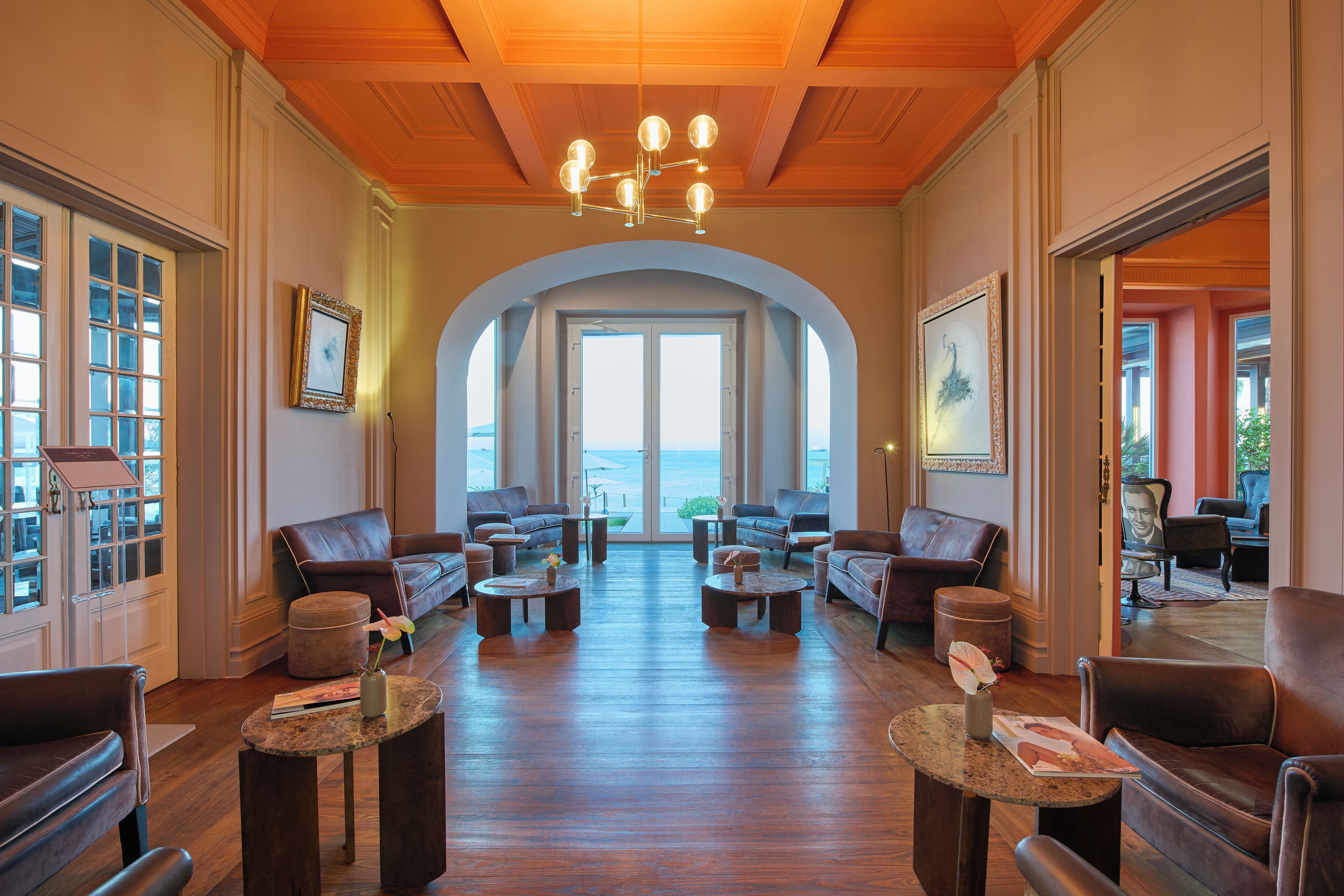 A spacious lobby with leather sofas, round coffee tables, and a large arched doorway leading to a balcony with a view.