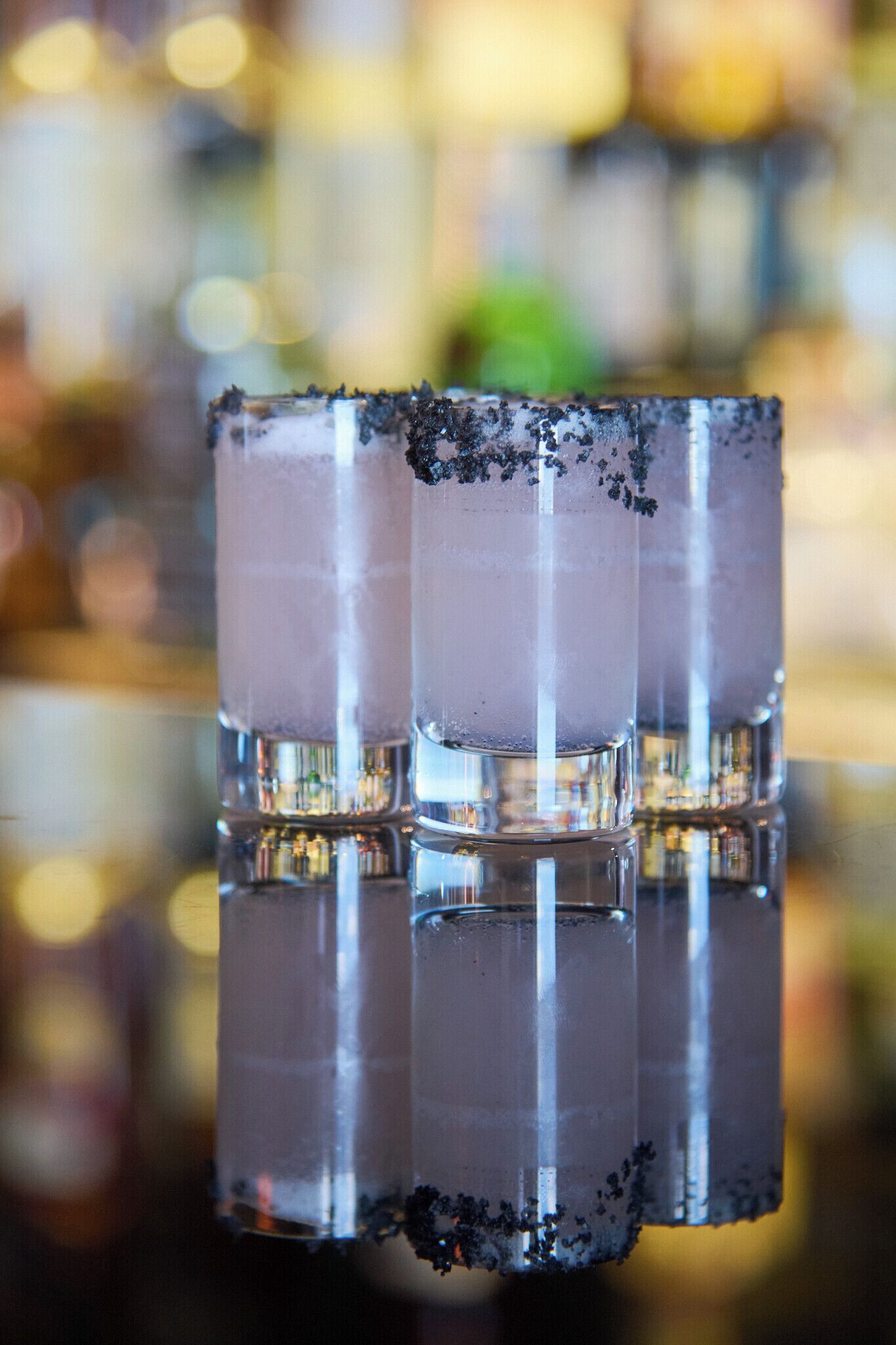 Un bar con tres vasos de un líquido transparente, posiblemente un cóctel, y cubitos de hielo.