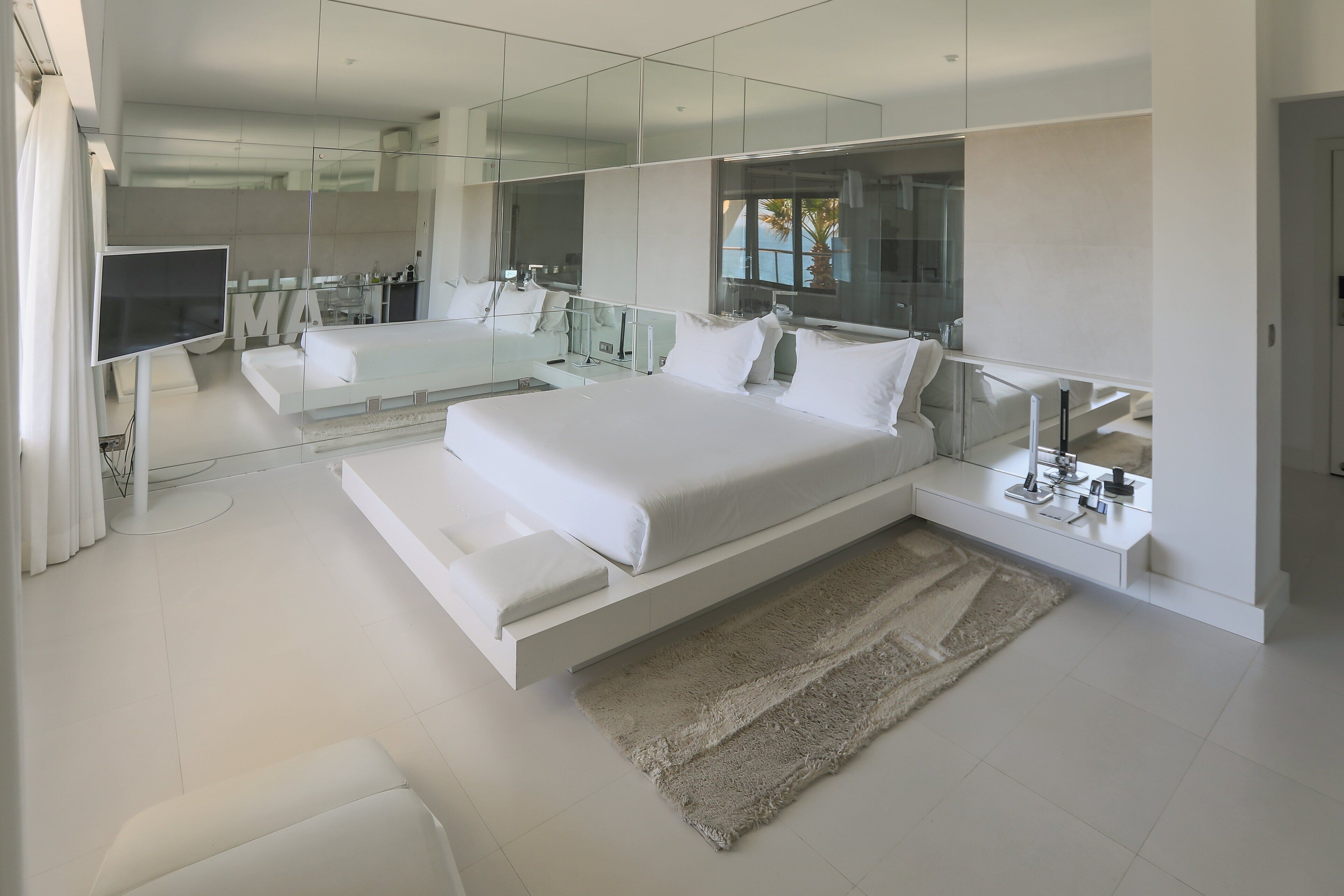 A modern bedroom with a large bed, a TV, and a glass-enclosed bathroom.