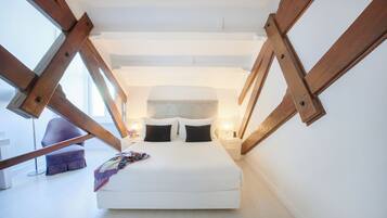 A bedroom with a large bed, wooden beams, a headboard, a nightstand, a lamp, and a purple chair.