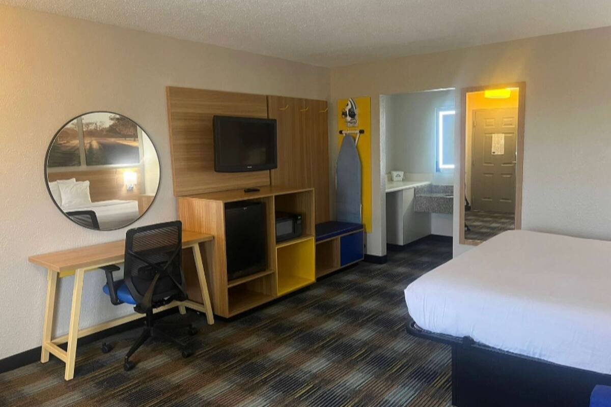 Habitación de hotel con una cama, un escritorio con silla, un televisor, un espejo y un armario.