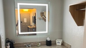Une salle de bain d’hôtel équipée d’un grand miroir, d’un lavabo, d’un distributeur de serviettes et d’une poubelle.