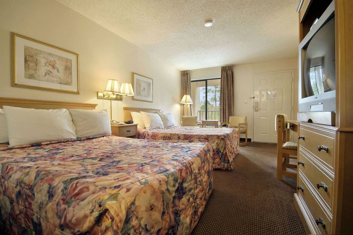Una habitación de hotel con dos camas, un escritorio, una silla, un aparador y una televisión.