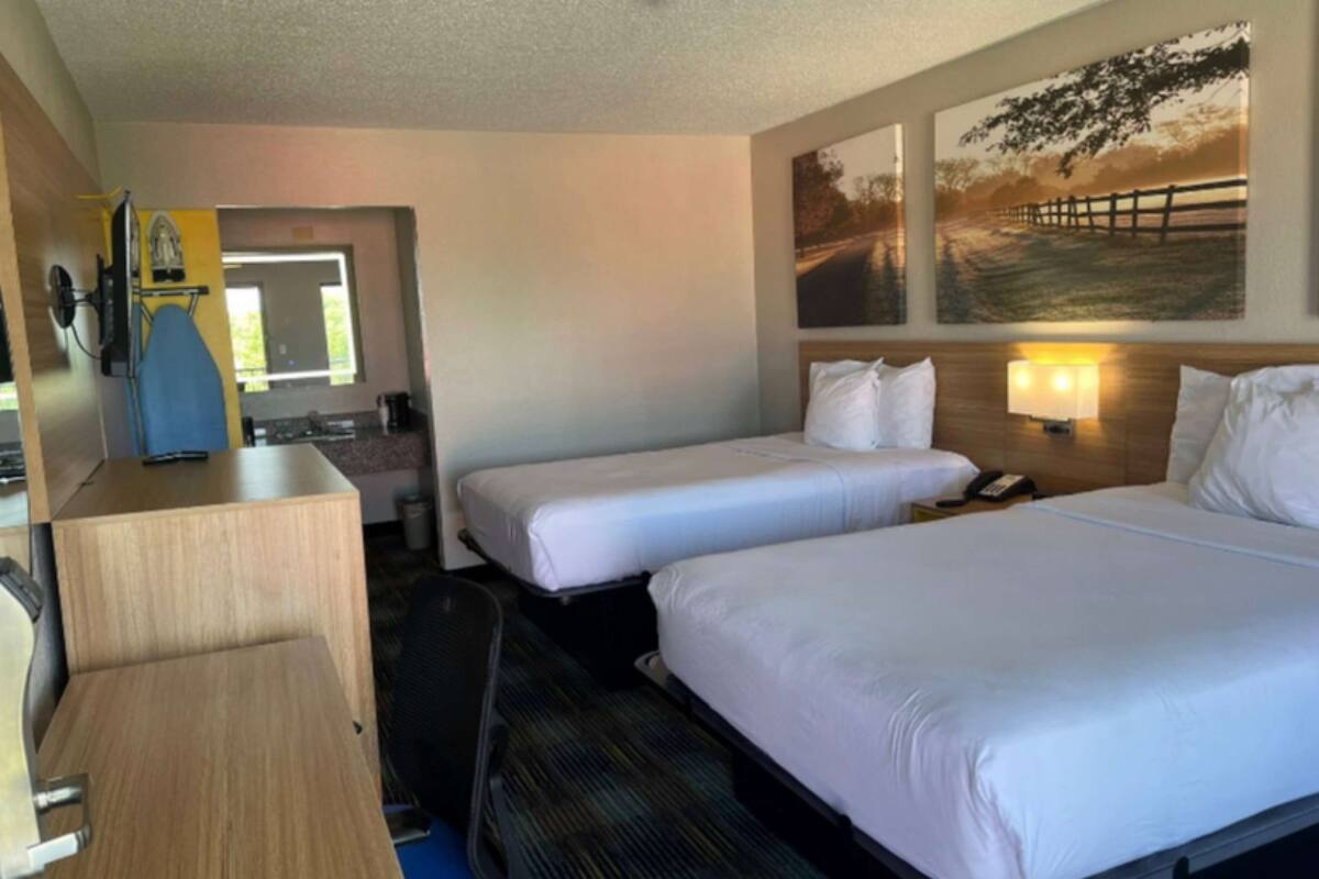 Habitación de hotel con dos camas individuales, un escritorio con silla, una mesita pequeña, un espejo y un televisor montado en la pared.