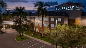 Een Courtyard by Marriott hotel met een modern design, met een verzorgd gazon, palmbomen en een parkeerplaats.