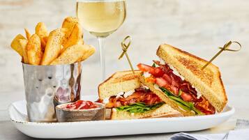 Un plato con un sándwich a la plancha, una copa de vino blanco y una taza de papas fritas.