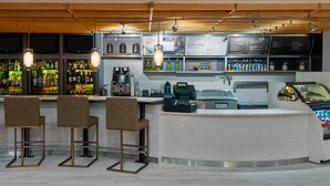 Een bar met een toonbank, drie barkrukken, een koffieapparaat en een menubord.