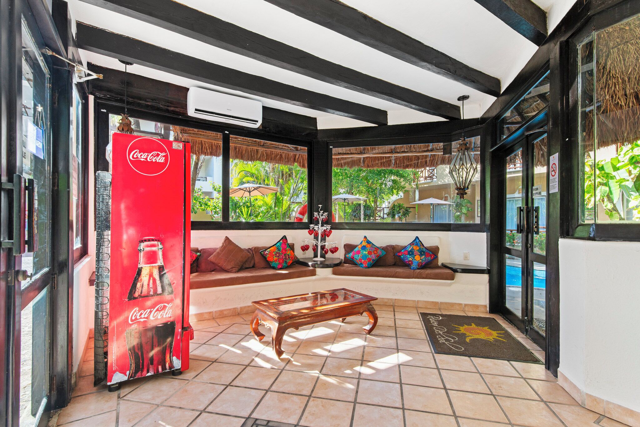Eine Lobby mit einer Couch, einem Glastisch, einem Coca-Cola-Kühlschrank und Blick ins Freie.