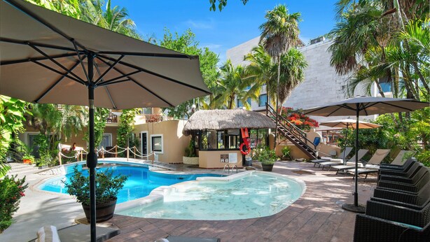 Un espace piscine aménagé avec des chaises longues, des parasols et une structure recouverte de chaume.