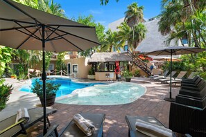 A pool area with lounge chairs, umbrellas, and a thatched structure. - Riviera del Sol (Playa del Carmen)