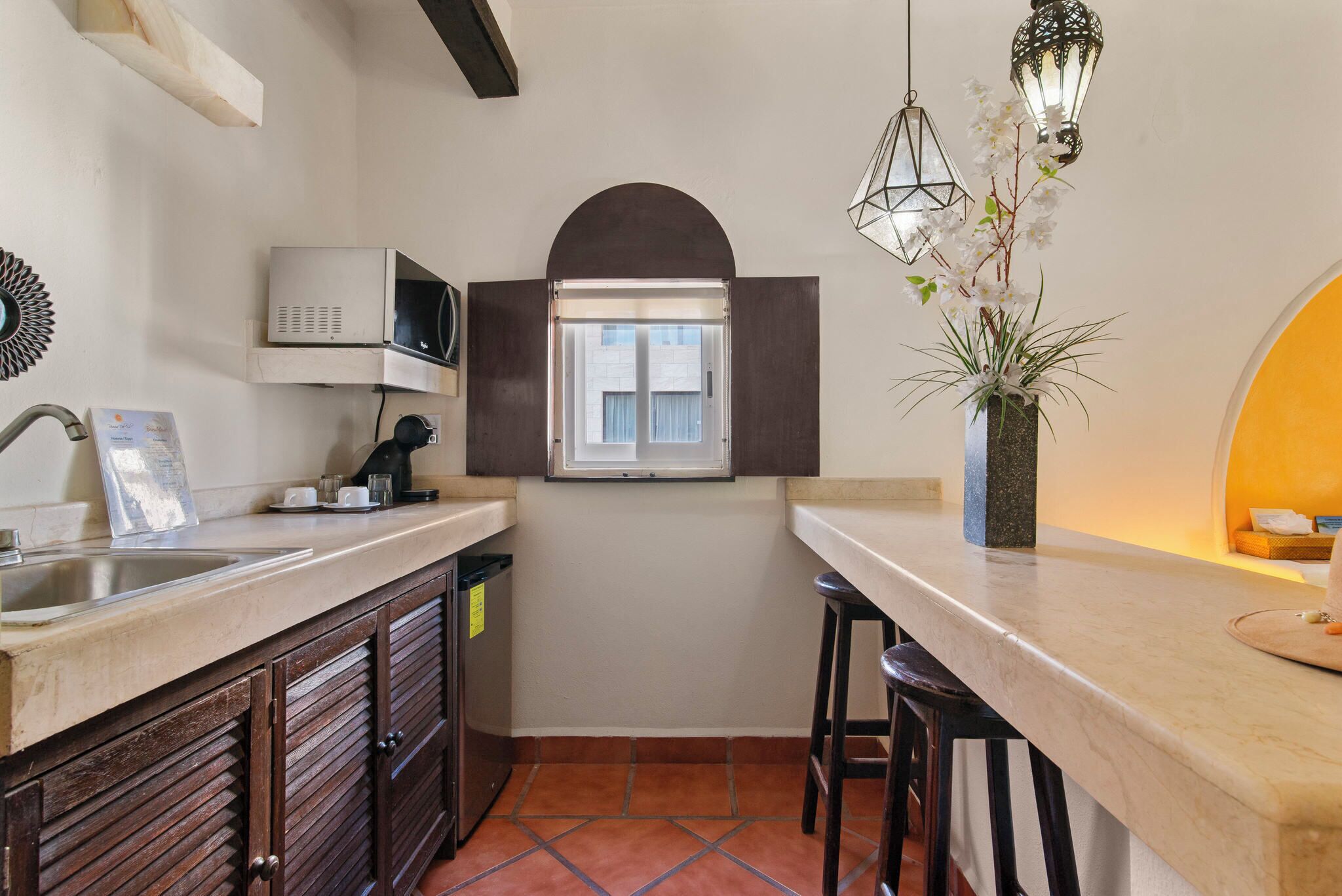 A compact kitchen with a microwave, sink, and a small window.
