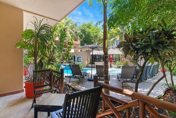 Un espace extérieur aménagé en patio, avec une piscine, des chaises longues et des plantes en pot.